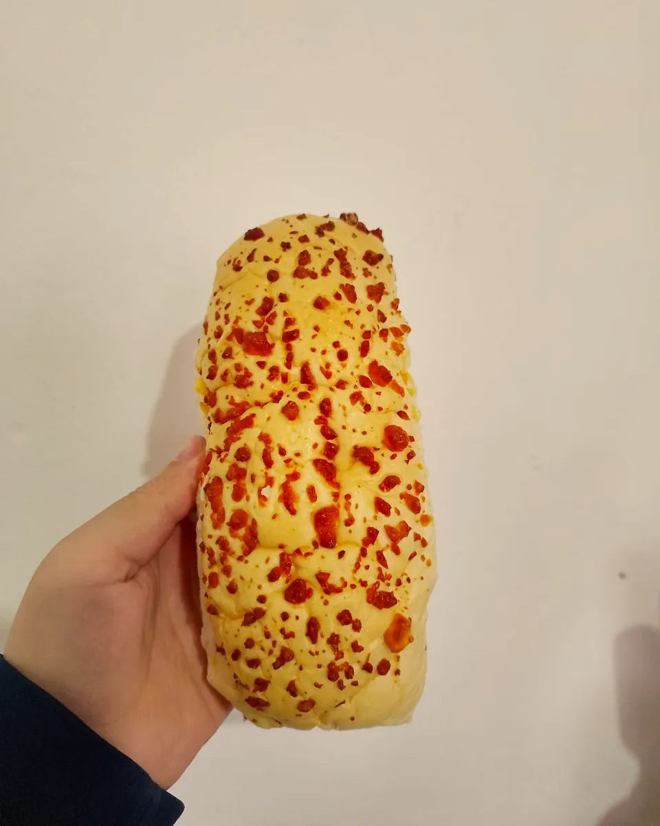 Mano sosteniendo un pan de lomo gratinado con queso de 20 centímetros